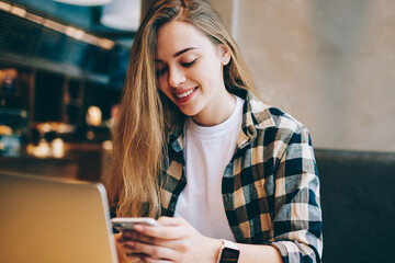 Cheerful female freelancer sharing information via laptop computer and smartphone using bluetooth...