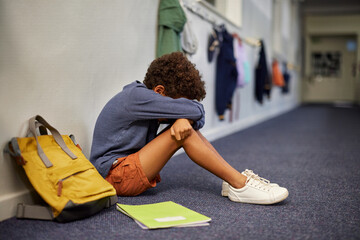 Depressed boy sitting on corridor floor at school