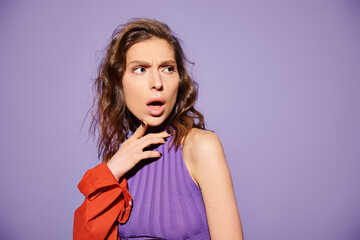 A stylish young woman with a surprised look on her face, dressed in vibrant orange attire against a...