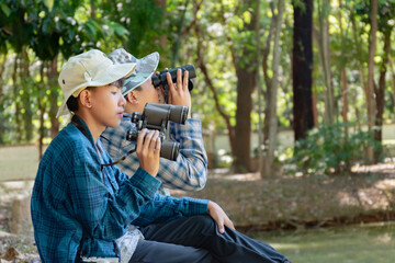 Obraz premium Asian children using binoculars to do the birdwatching in tropical forest during summer camp, idea for learning creatures, wildlife animals and insects outside the classroom.