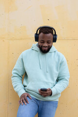 Happy black man listening music on phone with headphones isolated on yellow wall