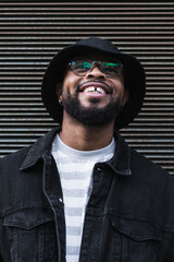 Obraz premium Waist up shot of happy black man smiles happily dressed in black hat and denim jacket being in good mood looking up expresses positive emotions