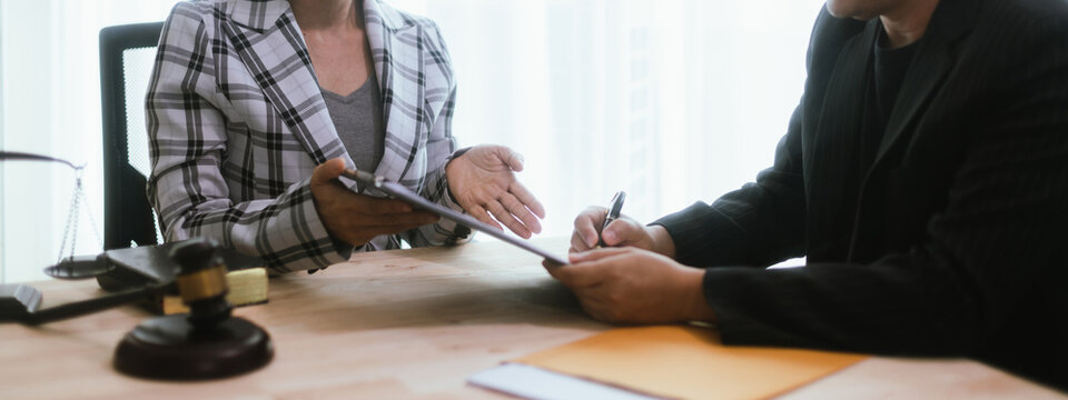 In a lawyer's office, a businessman consults an attorney for legal advice on a contract. The gavel symbolizes authority and justice. The lawyer explains the legislation and provides guidance on the ag