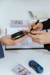 A customer signs a rental agreement for a new car at a dealership. The salesman explains the finance options and insurance details. With the paperwork complete, the keys are handed over, sealing the d