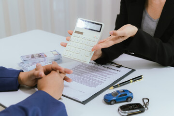 A salesman confidently explains the terms of an automobile purchase to a client. They review the...