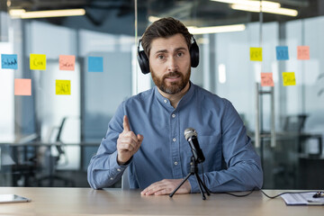 Confident man recording podcast in office setting with headphone and microphone