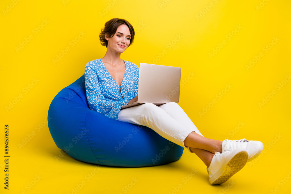 Poster full length photo of clever optimistic girl dressed print blouse sit on pouf typing email on laptop 