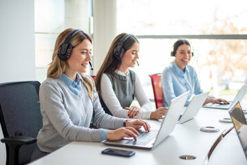 Blonde female customer service representative and her colleagues consulting clients online using headset. Call center and business people concept.