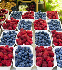 Small paper boxes with blueberries and raspberries displayed on street food market, closeup.