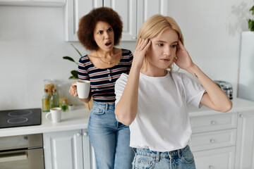 A lesbian couple stands in the kitchen, one holding a mug, the other holding her head, as they argue.