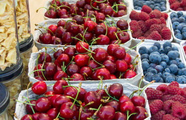 Small paper boxes with cherries blueberries and raspberries displayed on street food market, closeup.