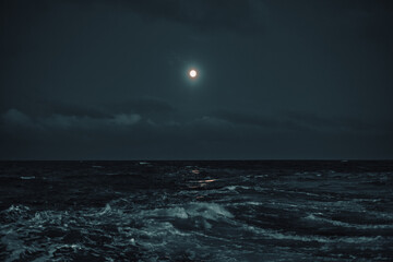 Full moon in the sky over the sea with waves at night.