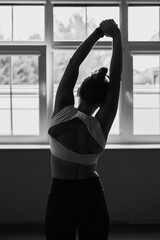 Fototapeta premium Joga, młoda dziewczyna wykonuje ćwiczenia rozciągające przed oknem. Kobieta praktykująca jogę. Rozciąganie, sport. Yoga, young woman practicing yoga, black&white, black and white photography. 