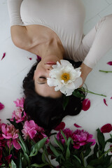 A beautiful woman lies on the floor and holds a flower to her face