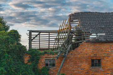 Damaged old brick animal barn. broken, collapsed, damaged roof in the building due to strong wind. a crumbling farm building in the countryside against the background of a beautiful morning sky in sum