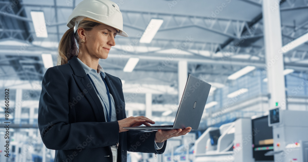 Poster Portrait of Caucasian Female Engineer in Hard Hat Standing and Using Laptop Computer at Electronic Manufacturing Factory. Technician Thinking About Daily Tasks and Working on Development Data.
