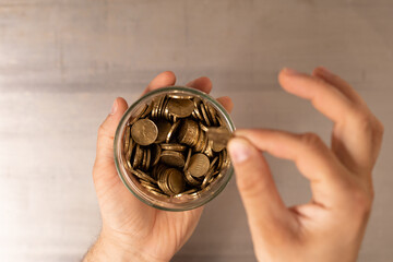 A hand holding a jar full of coins about to add another