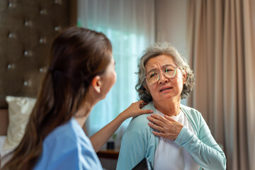 Obraz premium Asian woman doctor examine and consult senior patient on the bed in bedroom. Private duty nurse take care elderly woman suffering from shoulder pain at home. Home medical caregiving service concept.