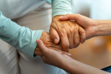Asian woman doctor consoling senior patient with holding her hand. Private duty nurse visit and take care elderly woman on the bed at home. Home medical caregiving service and health insurance concept