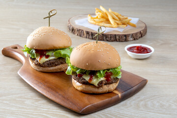 Two homemade burgers of beef, cheese and vegetables on an wooden table.