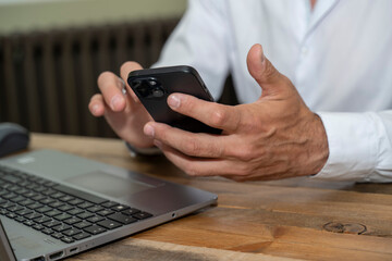 mains d'un homme tenant un téléphone à son bureau devant un ordinateur