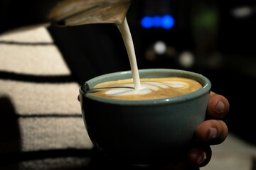 A barista draws a design on the milk froth of a coffee drink. Milk is poured into a cup of freshly brewed coffee. Close-up. High quality photo
