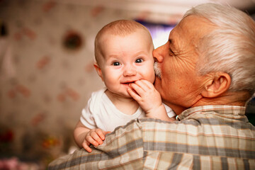 Elderly Man Kisses Baby Grandchild While Holding Them Indoors