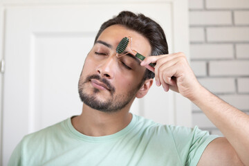 Young handsome man using jade roller for facial massage. Skin care and beauty concept 