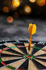 Close-up of a dart hitting the bullseye on a dartboard with bokeh light background, signifying precision and target achievement.