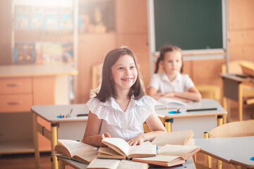 Cute girls are sitting in a classroom at a desk with notebooks and textbooks. The children listen carefully to the lesson. Back to school. School supplies. Student at a lesson, class during a lesson.
