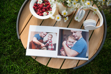 summer still life. Outdoor family photo album, headphones, daisies in a vase and raspberry berry on a plate lie on a table in the garden. family memories. happy summer holidays