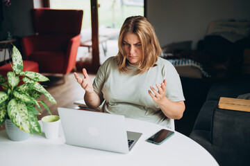Frustrated young adult woman looking in laptop computer in home, fling arms up. Negative people emotion