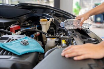 A young woman is filling the car's radiator with water, conducting a vehicle maintenance check