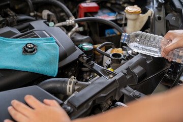 A young woman is filling the car's radiator with water, conducting a vehicle maintenance check