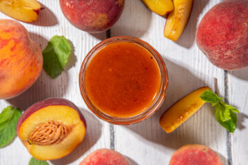 Homemade sweet sour peach chutney jam preserves with spices and raisins, in small jar, with fresh ripe peaches on white wooden table