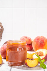 Homemade sweet sour peach chutney jam preserves with spices and raisins, in small jar, with fresh ripe peaches on white wooden table
