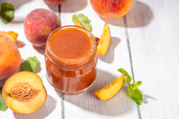 Homemade sweet sour peach chutney jam preserves with spices and raisins, in small jar, with fresh ripe peaches on white wooden table
