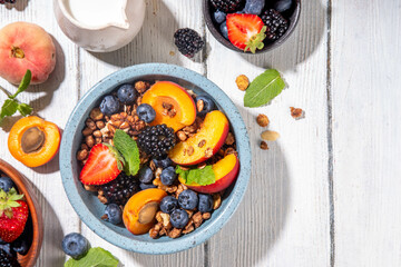 Granola breakfast with fruit and berry, summer whole grain tasty breakfast bowl with a lot of fruit and berries, with milk jug on white wooden table