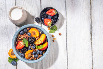 Granola breakfast with fruit and berry, summer whole grain tasty breakfast bowl with a lot of fruit and berries, with milk jug on white wooden table