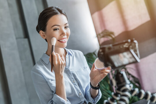 Social media influencer recording video tutorial on camera how to apply make up. Beauty blogger with makeup product recording online lessons for her channel course. Online content creator concept
