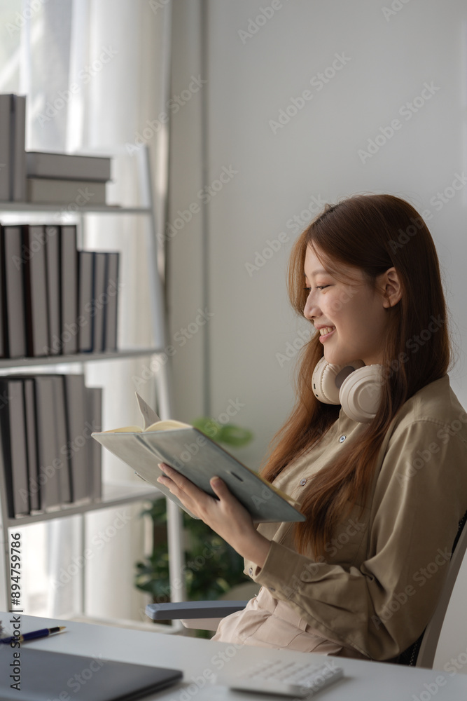 Wall mural an Asian businesswoman is writing detail from the last meeting, there is a beautiful employee is smiling in the workplace, taking a note into the book witch is the first draft of report