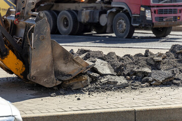 A large truck is pulling a large yellow bucket with a hole in the bottom