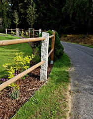 rural fencing made of hewn stove posts style enclosure in the mountains. a bed mulched with bark and perennial blue flowers along the edge