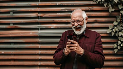 A senior man laughs while looking at his phone.