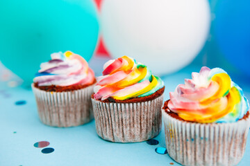 Rainbow cream cupcake or muffin on bright blue background with air balloons, celebration card