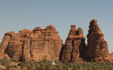 Fototapeta premium An oases of palm trees and a village with gigantic monoliths forming the backdrop