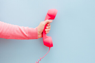 Communication and connection concept - woman hand with pink phone on light blue background