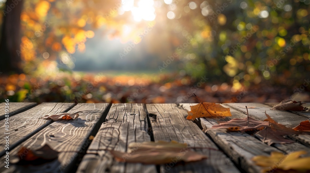 Poster A wooden table sits in a forest setting with fallen leaves scattered on the surface, with a background of blurred foliage and sunlight.