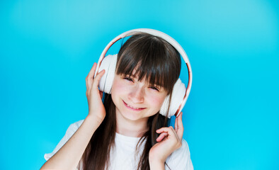 Cute teenage girl listens to music on wireless headphones. Little DJ on a blue background....