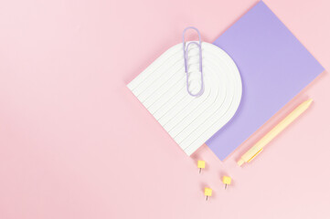 Top view of purple notebook, yellow pen, paperclip, pins, white arch tray on pink background....
